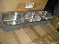 Close-up of one stainless steel triple bowl sink showing three bowls with drain holes and rounded edges.