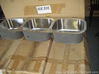 Five stainless steel triple sinks displayed outside their boxes, showing the sink basins and their three compartments.