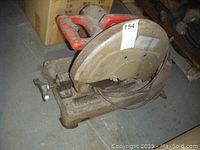 Side angle showing the large circular blade with protective cover and red handle, revealing dust and wear from use.