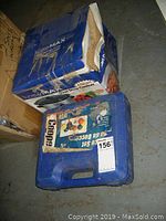 Photo showing blue boxed slow cooker and blue carrying case for bocce balls on floor.