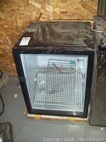 Front view of the Avanti wine fridge showing glass door and wire shelves inside. Top surface has dust and dirt.