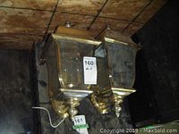 Two brass-finish outdoor coach light fixtures mounted vertically, showing front and side views with tags attached.