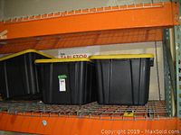 Three black storage totes with yellow lids stacked on an orange metal shelf.