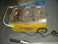 Front and top view of yellow hot dog cart showing three stainless steel compartments with lids, handle and power cord.