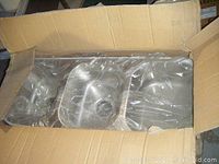 Photo of one stainless steel triple sink inside an open cardboard box with plastic wrap covering it, showing three separate bowls and drain holes