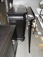 Side view of black dresser with carved edges and bun feet next to matching mirror frame.