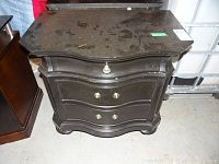 Front view of one black wooden night table showing two drawers with brass handles, some handles missing, dusty surface