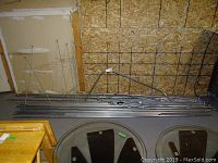 Multiple straight galvanized pipes and rods stacked against OSB wall with round tables in foreground