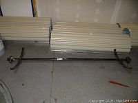 Full view of the trailer axle laid on the floor showing overall length and attached leaf springs at each end.