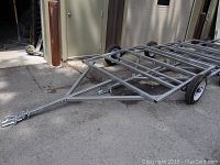 Full view of galvanized steel trailer frame with crossmembers and two axles with wheels.
