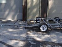Side angle view of the galvanized steel trailer frame parked on asphalt beside a building.