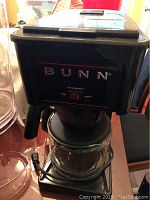 Front view of black Bunn coffee maker with glass carafe on warming plate and power switch on front panel.