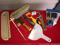 Painting tools laid out on a red surface including various brushes, rollers, scrapers, and plastic tools.