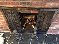 Photo showing metal mesh fireplace screen with two andirons in front.