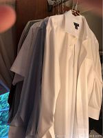 Photo of a subset of men's dress shirts hanging on a rack featuring white, gray, and light-colored shirts.