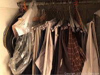 Photo showing 30 pairs of men's pants hanging on a rack in a closet. Pants vary in color and style, including dress and casual pants.