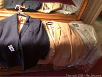 Seven men's sports coats in various colors, sizes XL, hanging on a reflective surface. Includes black, tan, beige coats.