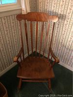 Full view of the solid pine wooden rocking chair placed in a corner near a window with floral wallpaper.