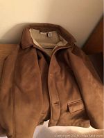 Brown men's shearling coat folded on bed showing overall front and collar.