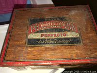 Top view of the wooden cigar box showing the Philadelphia Perfecto branded label with the text 'It's Ripe Tobacco!' worn from use.