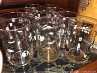 Photo of 10 clear mid century glasses with white decorative motifs in varied patterns showing a retro style on a dark marble surface.