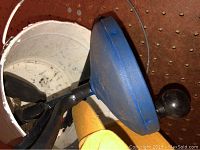 Blue rubber drain cleaner plunger with black handle sitting inside a white bucket, showing usage marks.