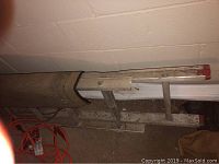Photo of an aluminum extension ladder, shows middle section and some surroundings with dirt and concrete floor.