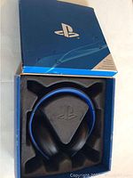 Top view of the PlayStation Bluetooth headset inside the original blue PlayStation branded box with some visible wear.