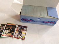 Photo of the open box with many stacked hockey cards inside and two individual hockey cards laid in front showing player images and design