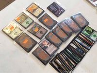 Sealed packets of Magic The Gathering trading cards arranged in rows along with some loose cards in sleeves on a white surface.