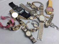 Photo showing an assortment of men's and ladies watches in various styles, colors, and bands placed on a flat surface.