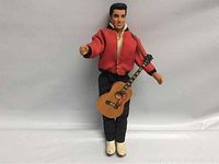 Front view of Elvis Presley doll in red jacket and black pants holding guitar.