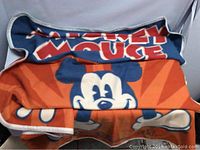 Close-up of the plush Mickey Mouse blanket with large character graphic and bold text on orange and blue background.