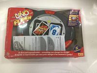 Front of the Uno Flash card game box showing the electronic spinner, cards, and instruction manual inside plastic viewing window. Box is red with visible wear.
