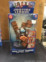 Front view of the packaged Justice League Power Escape Superman figure, showing figure and accessories in sealed box.
