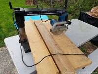 Full view of the Ryobi radial arm saw mounted on a thick wooden board with power cord visible.