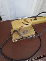 Top view of vintage Black and Decker finishing sander showing the yellow body and power cord coiled around it.