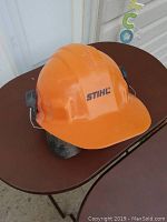 Front and side view of orange Stihl safety helmet showing ear protection and logo.