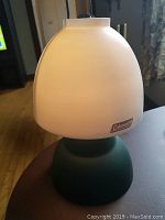 Full view of Coleman camping lantern showing the white opaque globe and green base on a table.