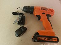 Black and Decker cordless drill lying on table with detachable battery and wired charger.