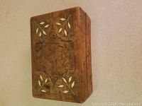 Teak wood box with visible carved flower design and mother of pearl leaf inlay on the top panel in angled side view.