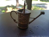 Close-up of a small brass-colored miniature watering can, showing handle and spout.
