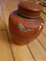 Side view showing reddish lacquered tea tin with hand-painted butterfly on curved surface.