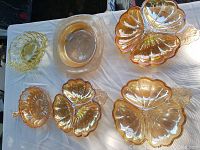 Top-down view showing all six carnival glass pieces arranged on a white cloth. The iridescent amber coloration is visible with reflectiveness typical of carnival glass.