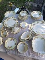 Full view of the entire set spread out on a table showing plates, platters, bowls, gravy boats and other items with floral decoration and gold trim.