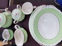 Top view of the assembled set items including teapot, sugar bowl, milk jug, various sizes of plates and trays with green, white and gold detailing.