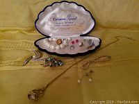 Photo showing entire collection of jewelry in a clam shell style box and displayed around it, includes pearl necklaces, rings with pink and pearl stones, and rhinestone brooch.