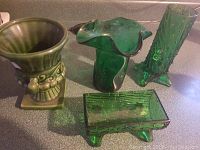 Four vintage green glass decorative items arranged on a flat surface: three vases of varying styles and one rectangular bowl.
