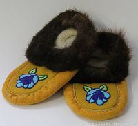 Full view of the moccasins showing the fur-trimmed opening, suede body, and beadwork floral designs on the front.