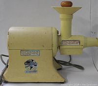 Side view of the heavy duty juicer showing the base motor housing, feed chute with wooden pusher, and juice outlet spout.